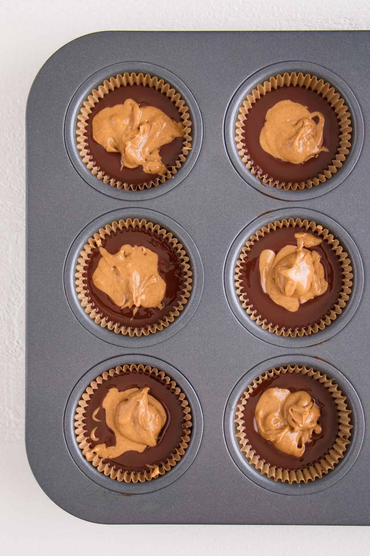 a muffin tin lined with melted chocolate and peanut butter dollops