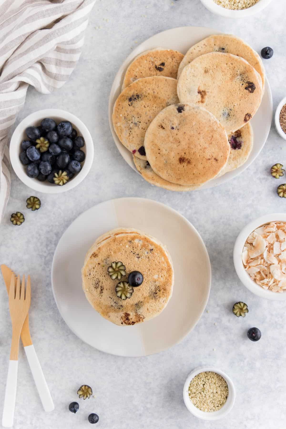 two plates surrounded by berries, hemp seeds, and coconut flakes