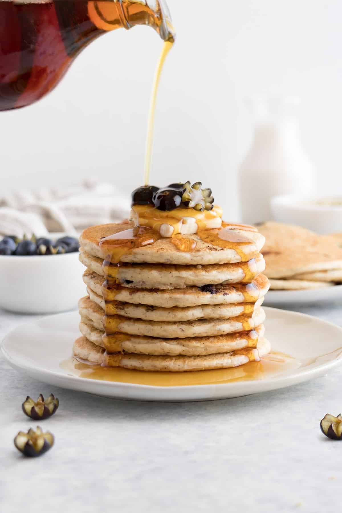 pouring maple syrup over a stack of vegan blueberry pancakes