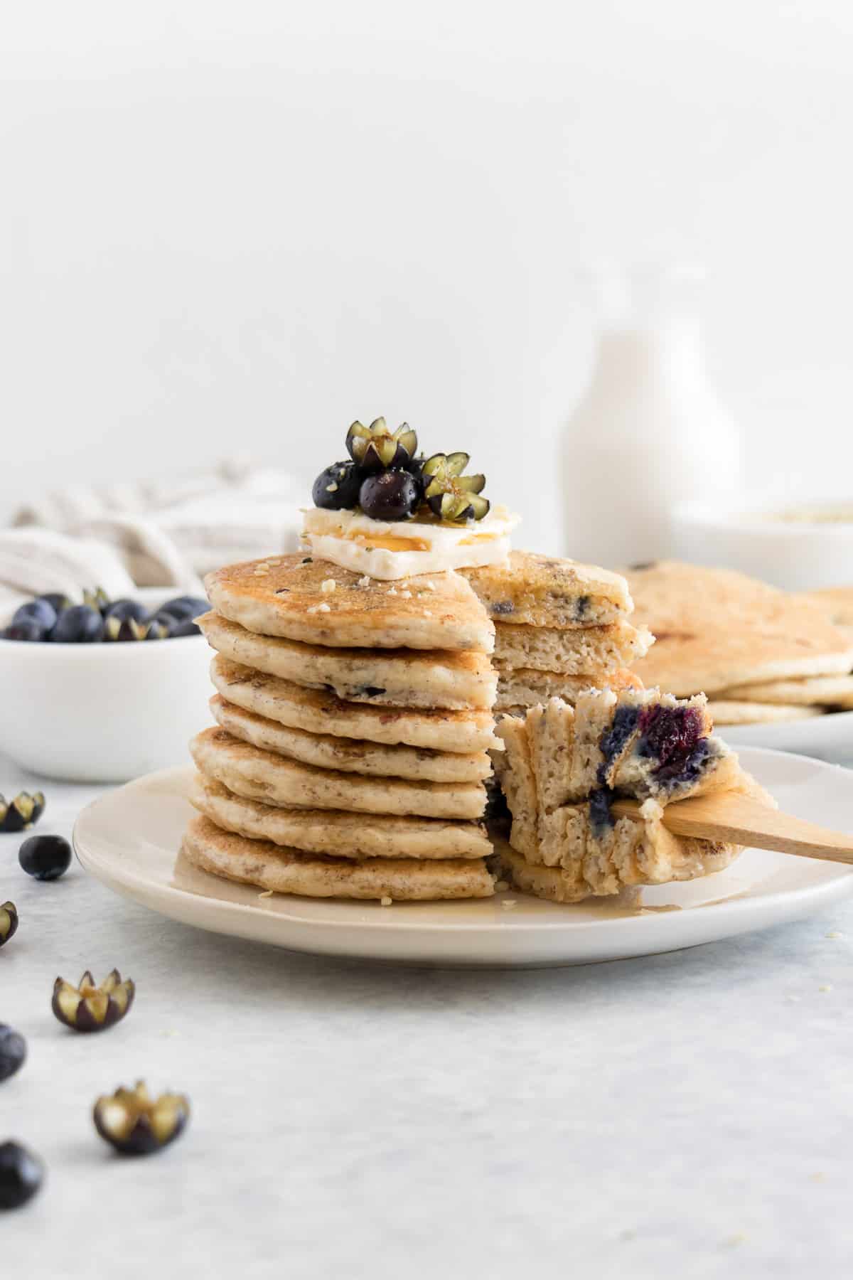 a fork slicing through a pancake stack with almond milk in the background