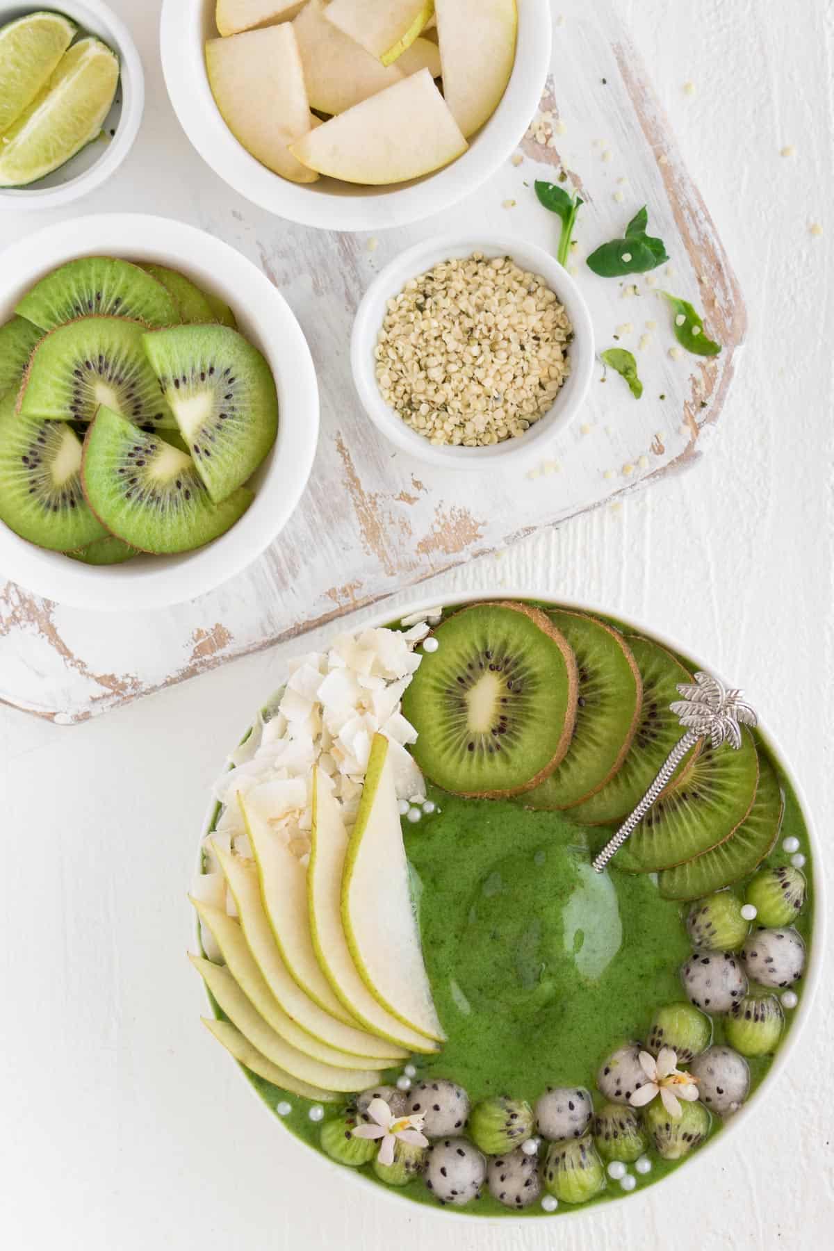 green smoothie bowl with the ingredients sitting on a white distressed cutting board