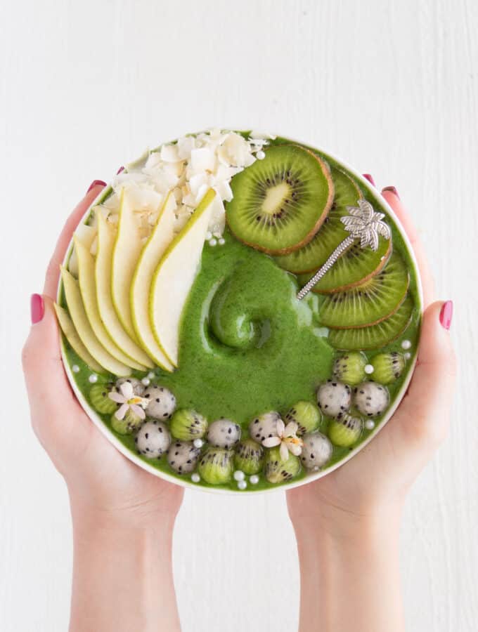 two hands holding a kiwi and pear smoothie bowl