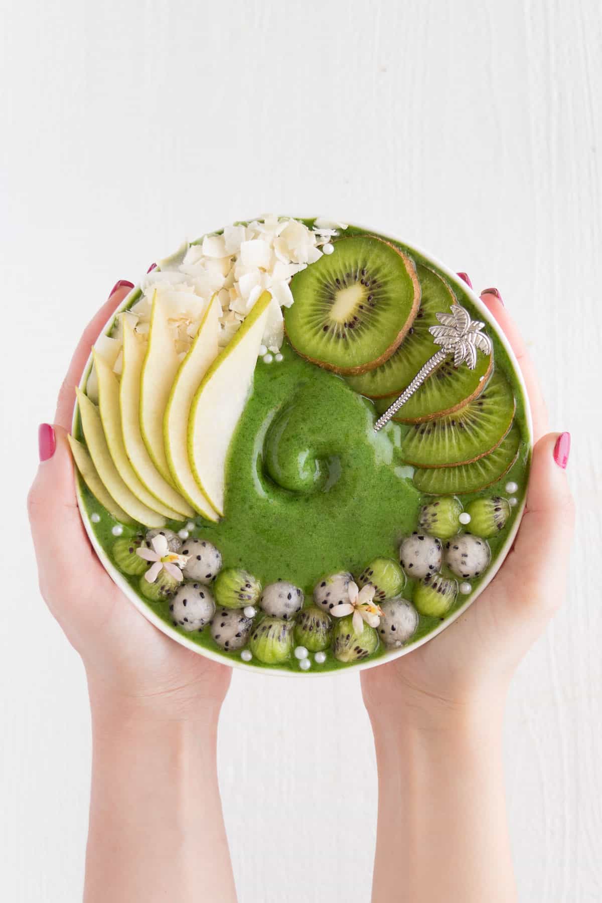 two hands holding a kiwi and pear smoothie bowl