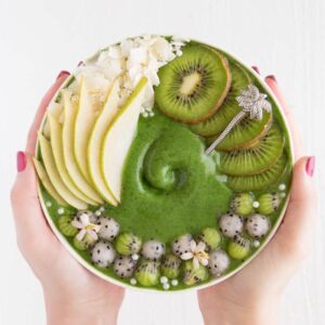 two hands holding a green smoothie bowl