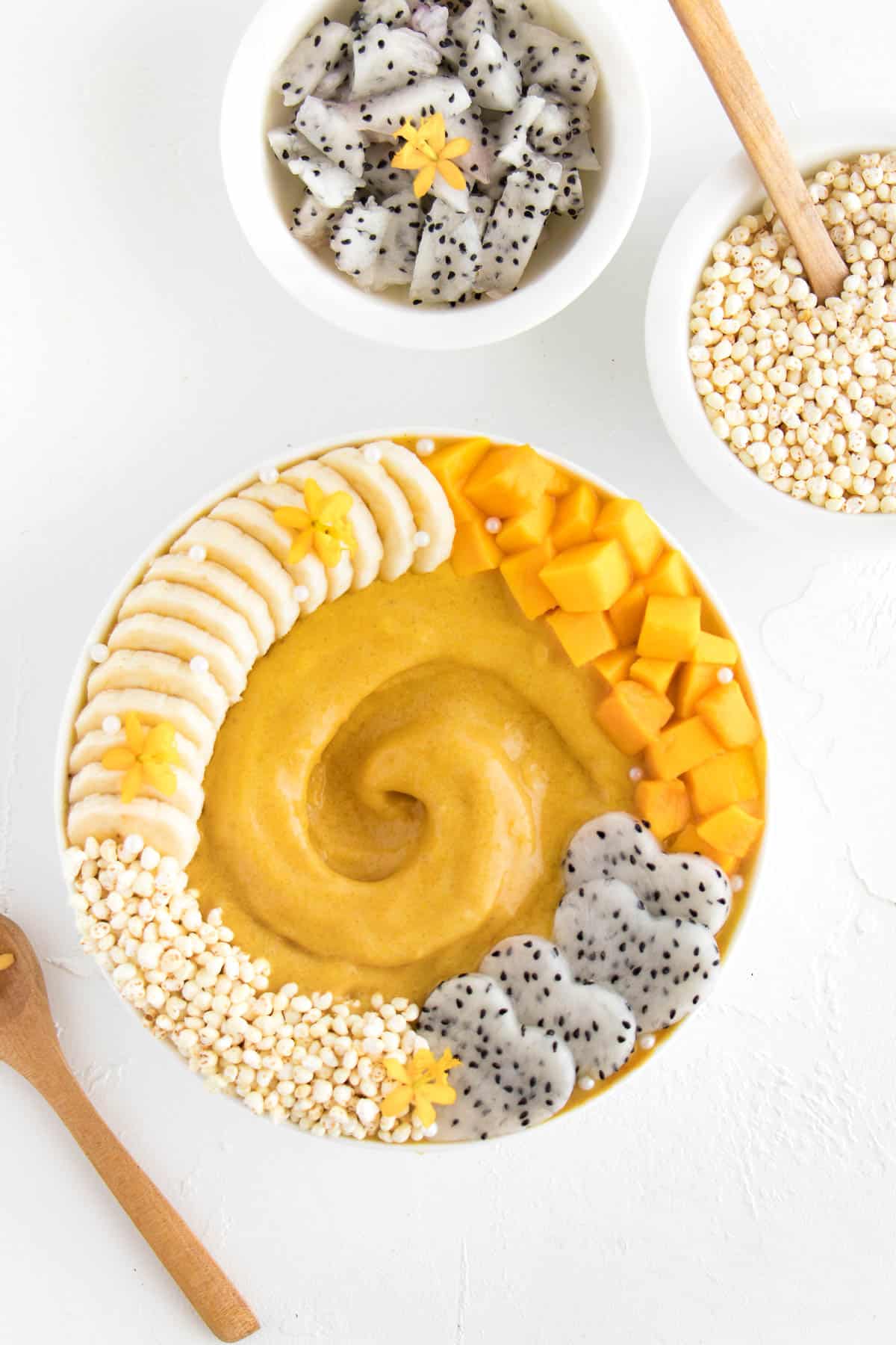 yellow smoothie in a bowl with banana, mangoes, dragon fruit, and puffed millet