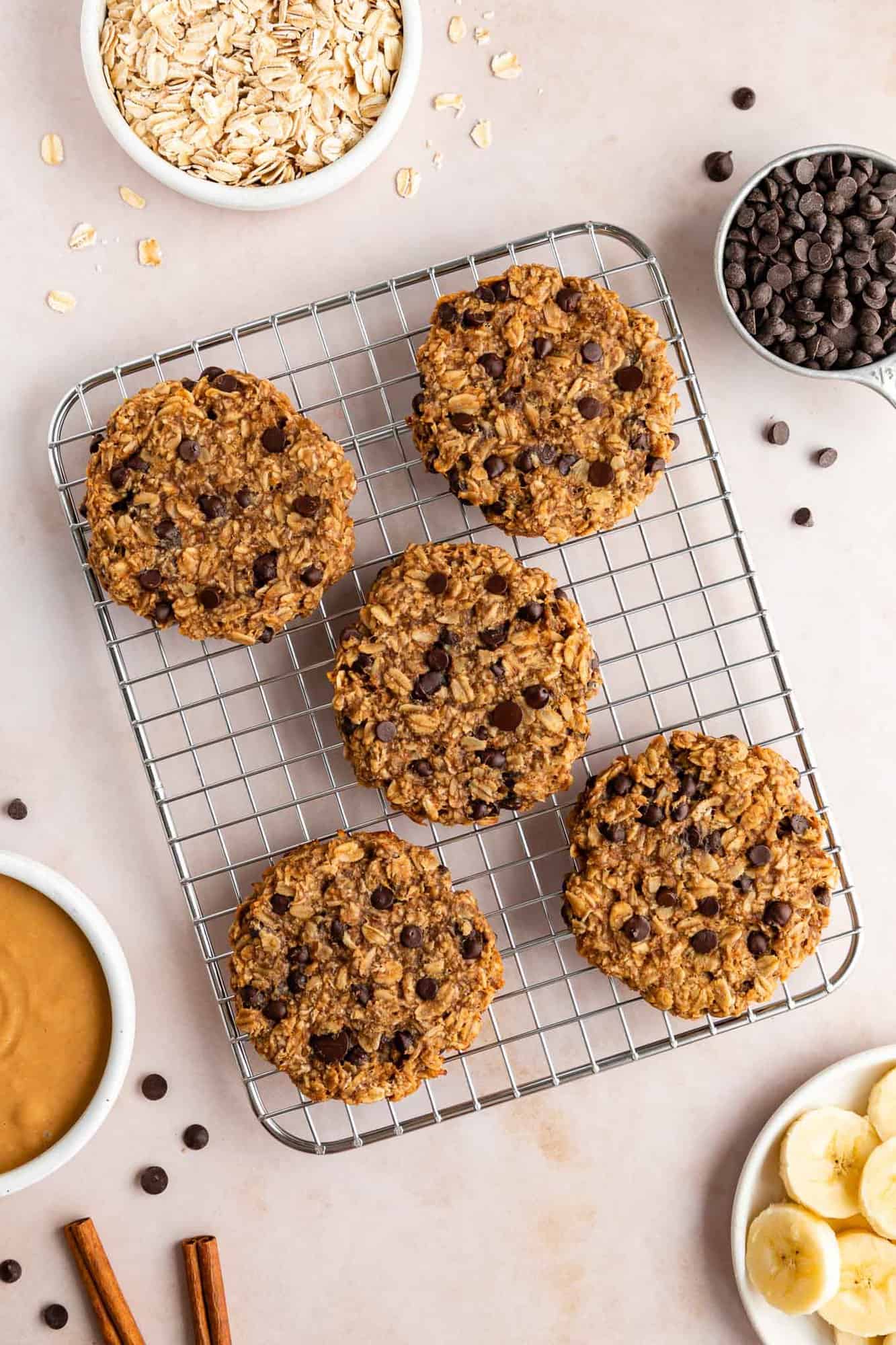 five peanut butter banana oatmeal cookies on a wire cooling rack surrounded by bowls of ingredients