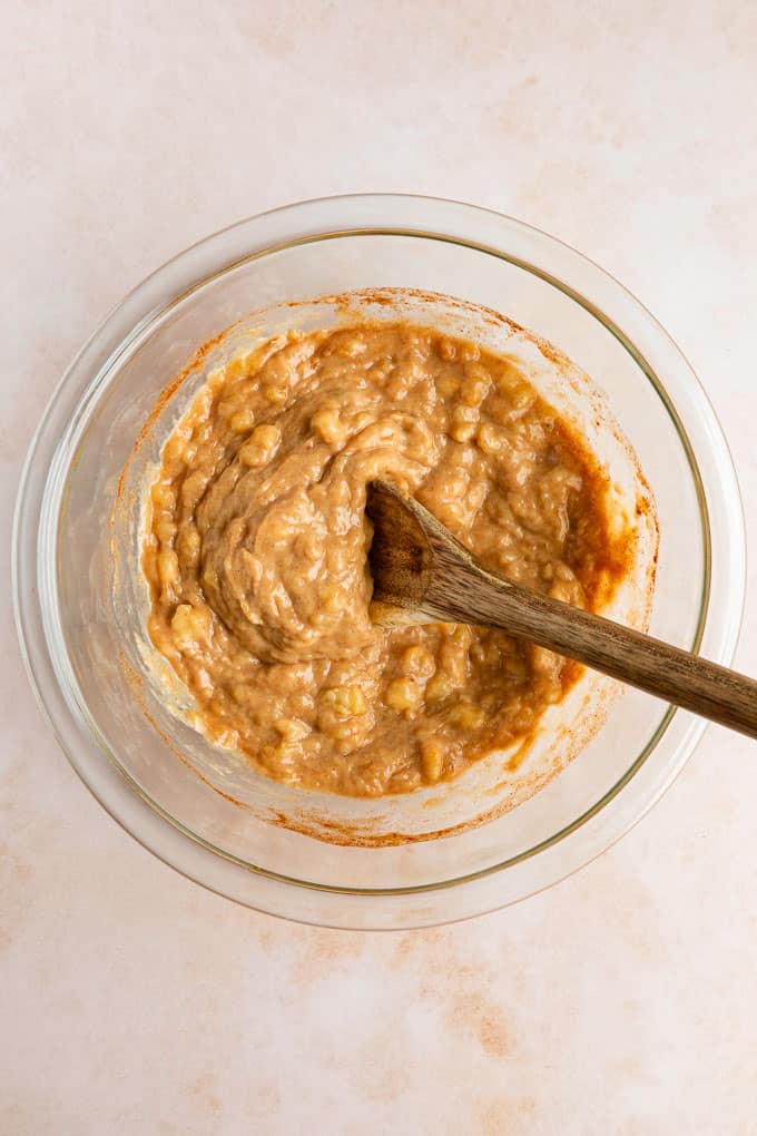 a wooden spoon mixing peanut butter and mashed banana in a glass bowl