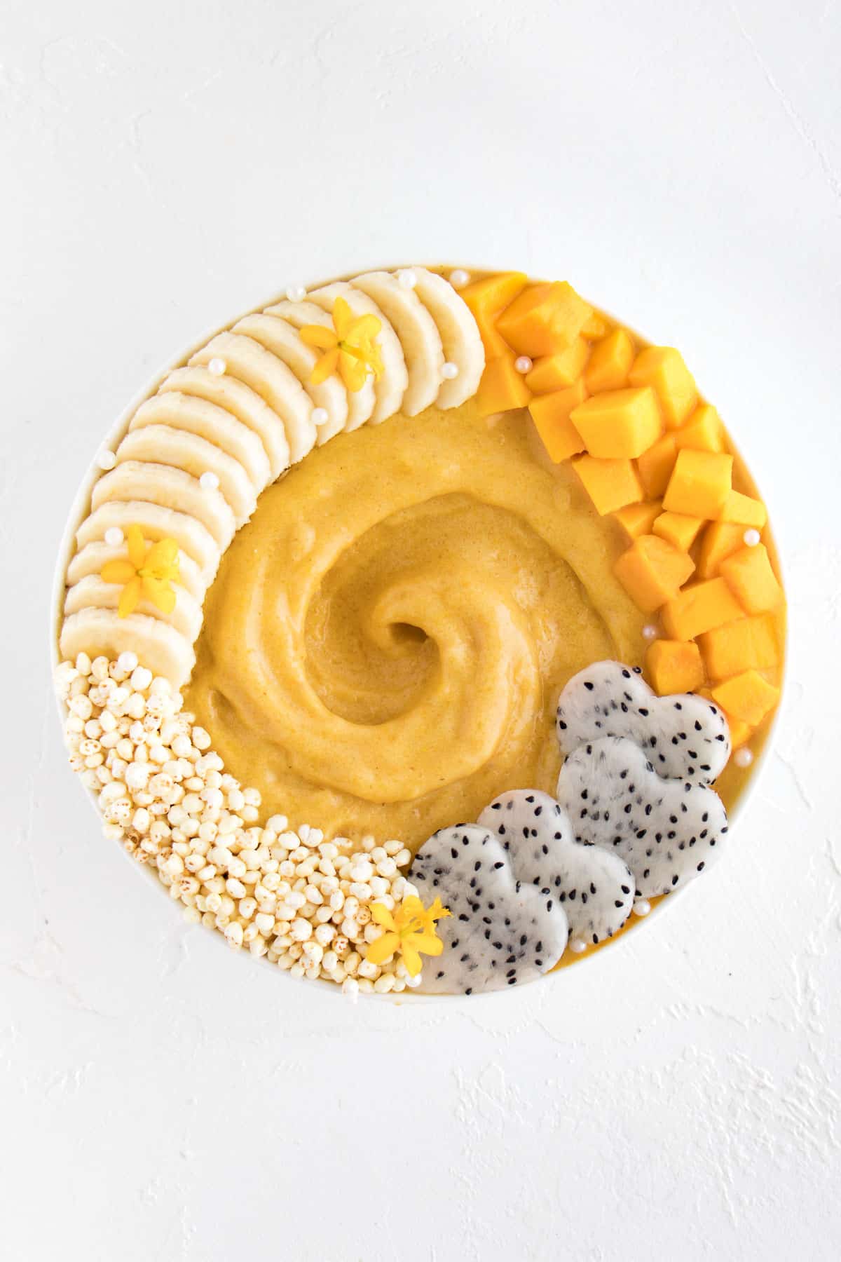 yellow smoothie in a bowl with mango, banana, and dragon fruit on top