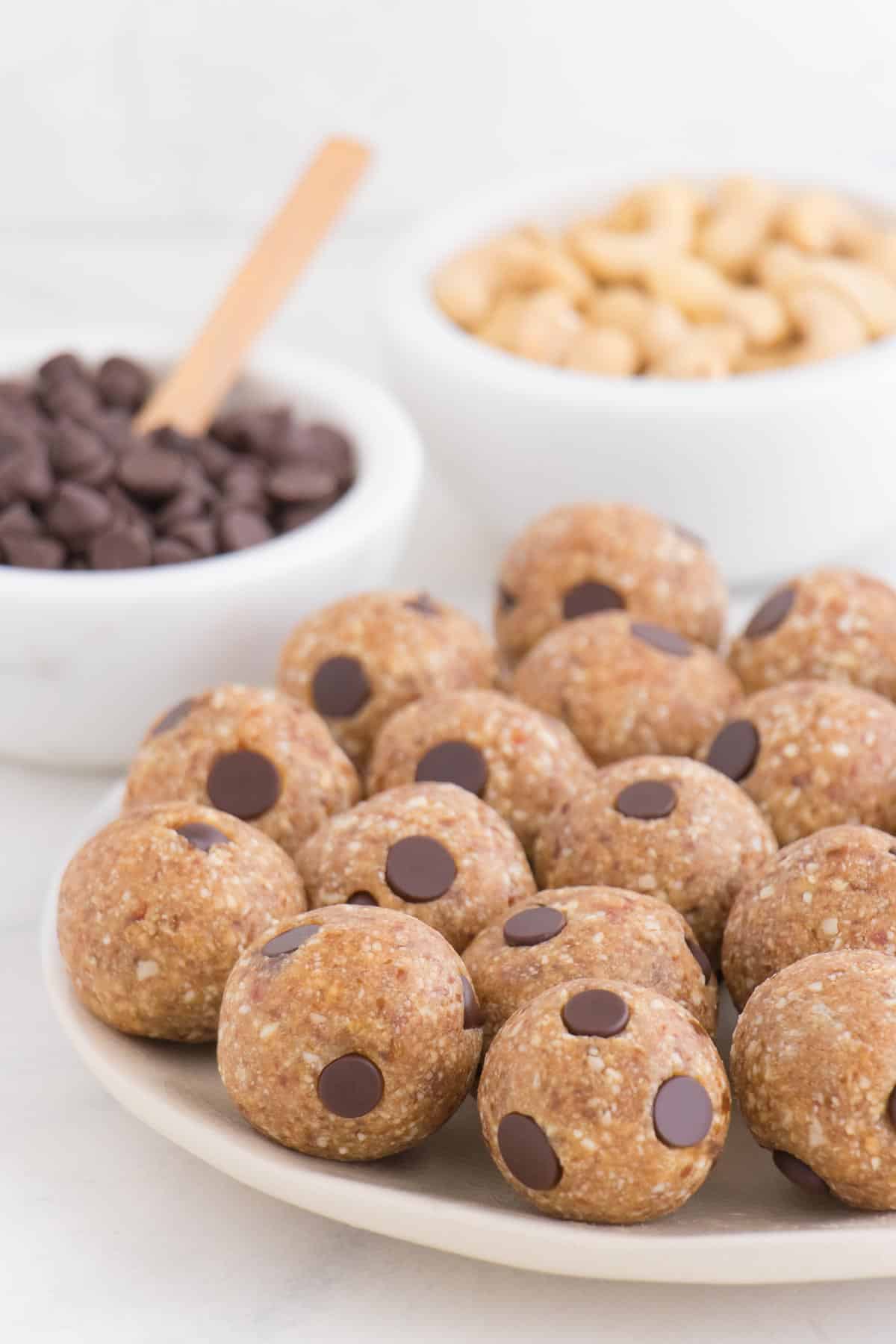 balls of cookie dough on a plate in front of chocolate chips and cashews