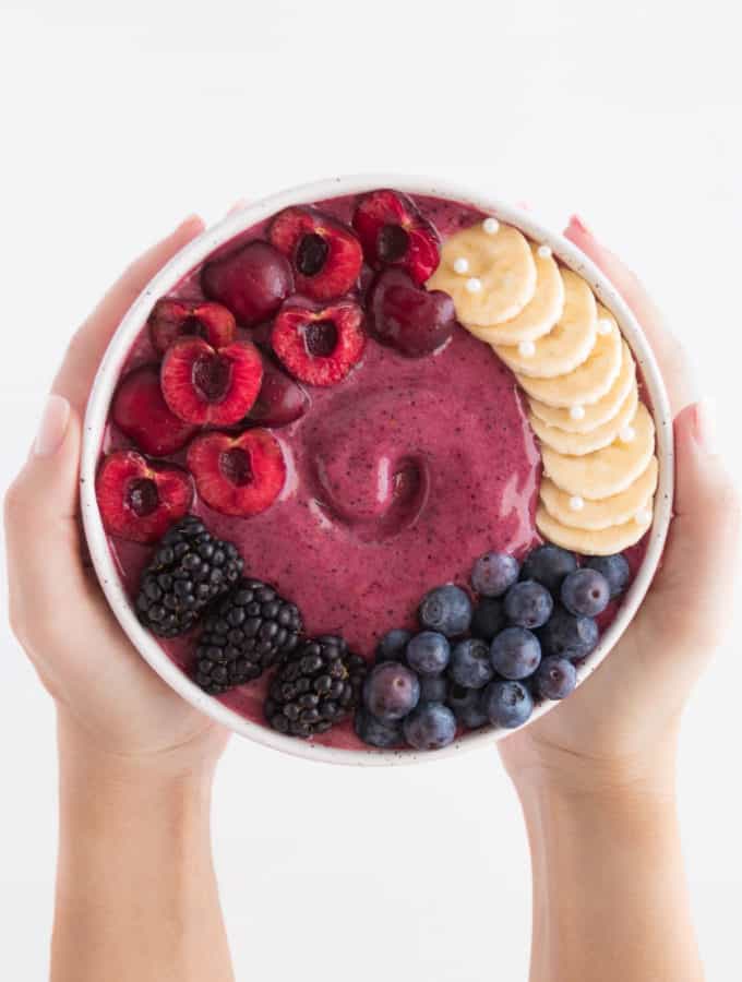 two hands holding a cherry berry smoothie bowl