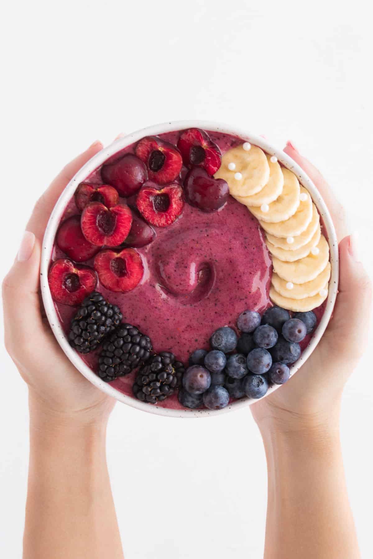 two hands holding a cherry berry smoothie bowl