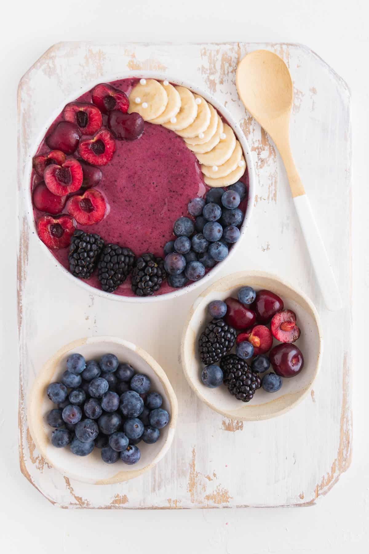 cherry smoothie bowl on top of a white distressed cutting board alongside small bowls of fruit