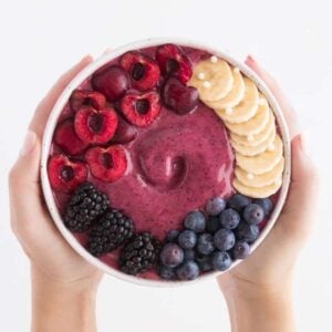 two hands holding a cherry berry smoothie bowl