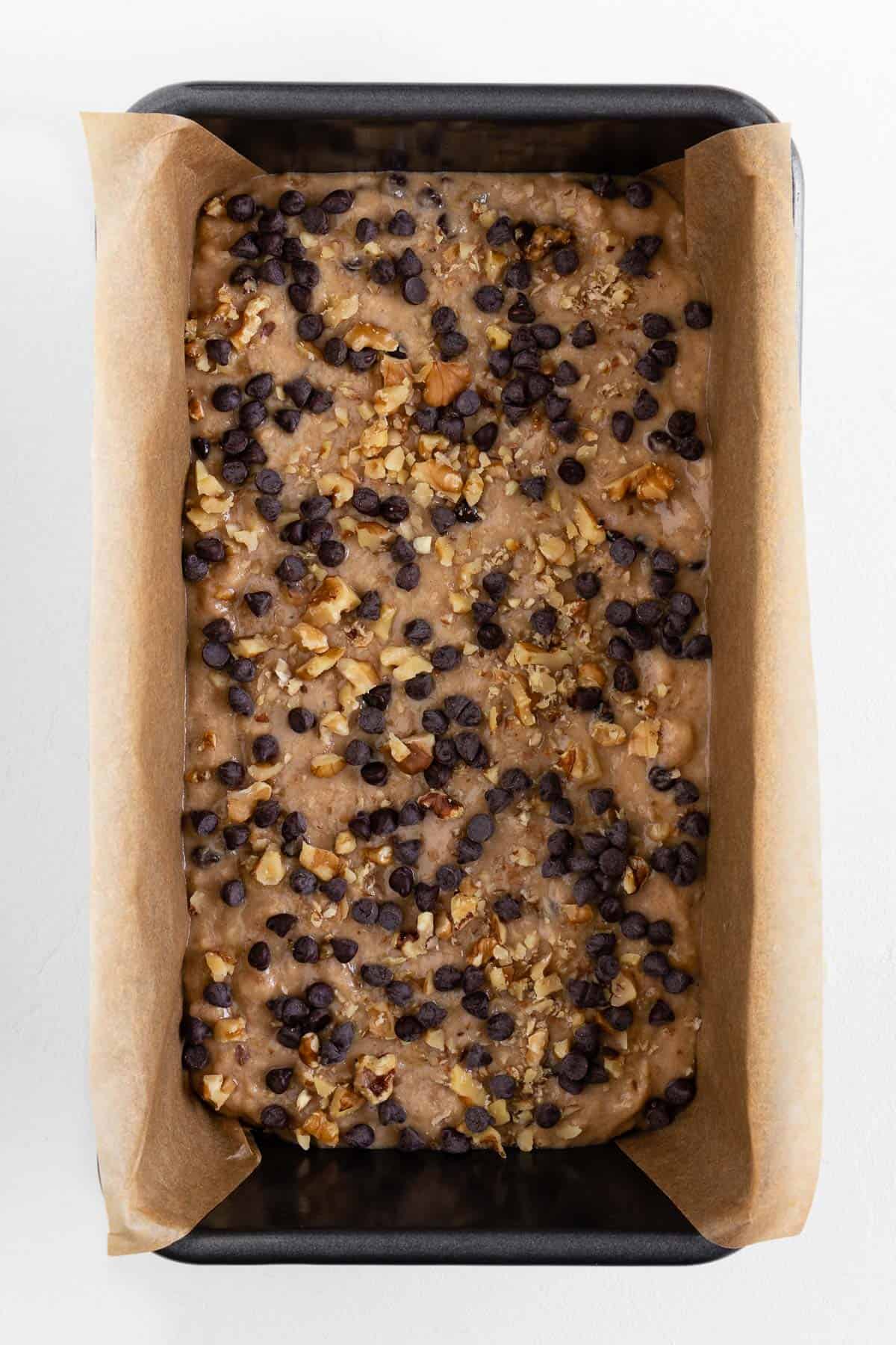 banana bread batter inside a loaf pan topped with crushed walnuts and chocolate chips