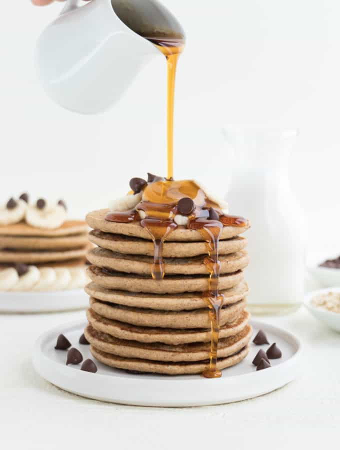 pouring maple syrup over a stack of vegan chocolate chip banana pancakes