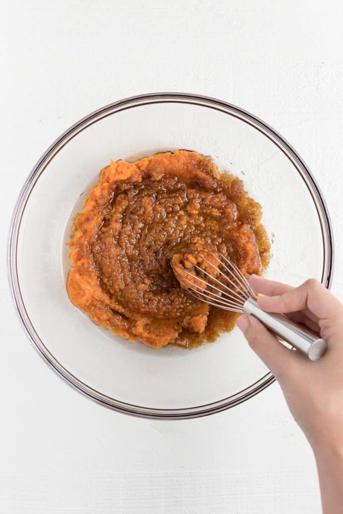 a hand whisking together pumpkin, brown sugar, coconut oil, and almond butter