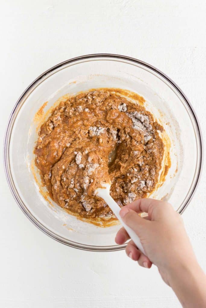 hand mixing pumpkin bar batter in a large glass bowl