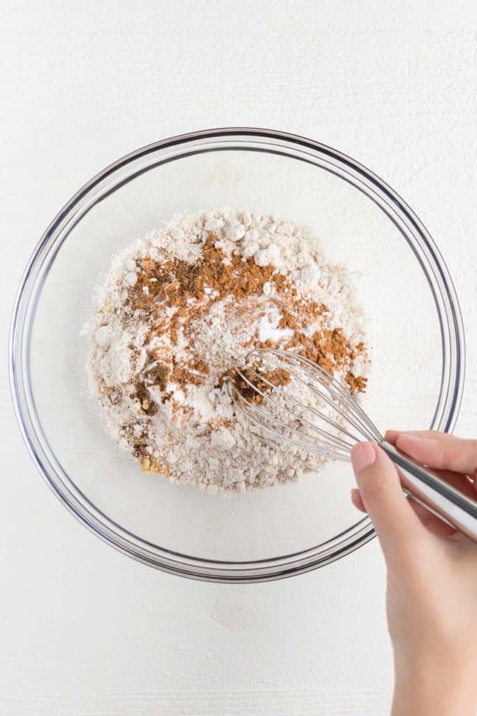 whisking together flour, cinnamon, nutmeg, allspice, cloves, and ginger in a large pyrex bowl