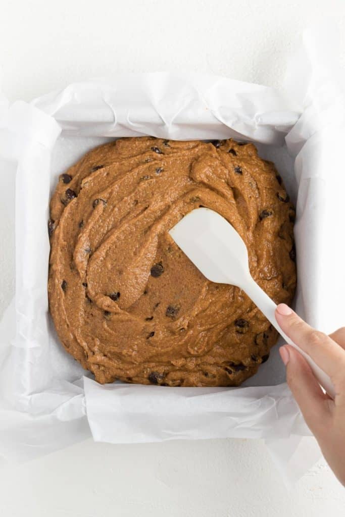 a hand spreading pumpkin bar batter into a square pan