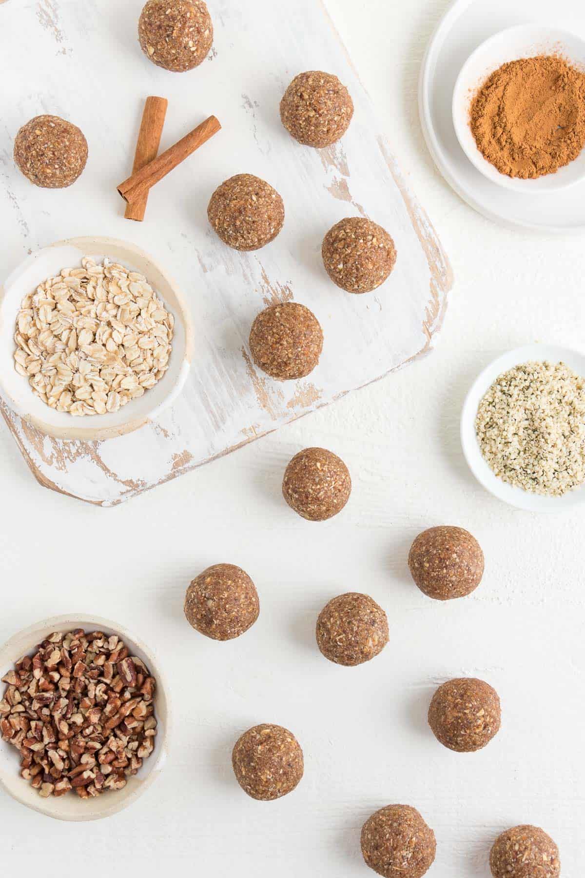 bliss balls on a white distressed cutting board alongside oats, pecans, and hemp seeds