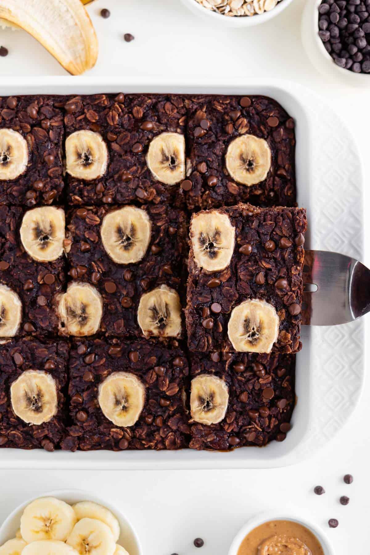 a spatula lifting a slice of vegan chocolate banana baked oatmeal out of a white baking dish