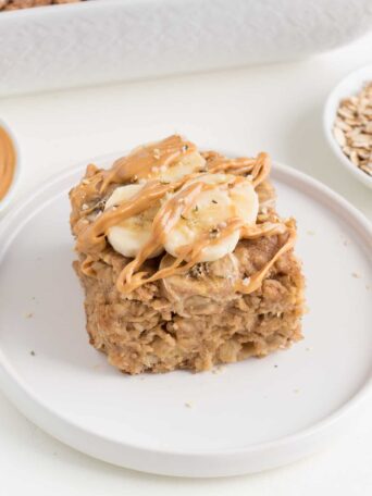 slice of peanut butter banana baked oatmeal topped with sliced bananas and peanut butter on a white plate