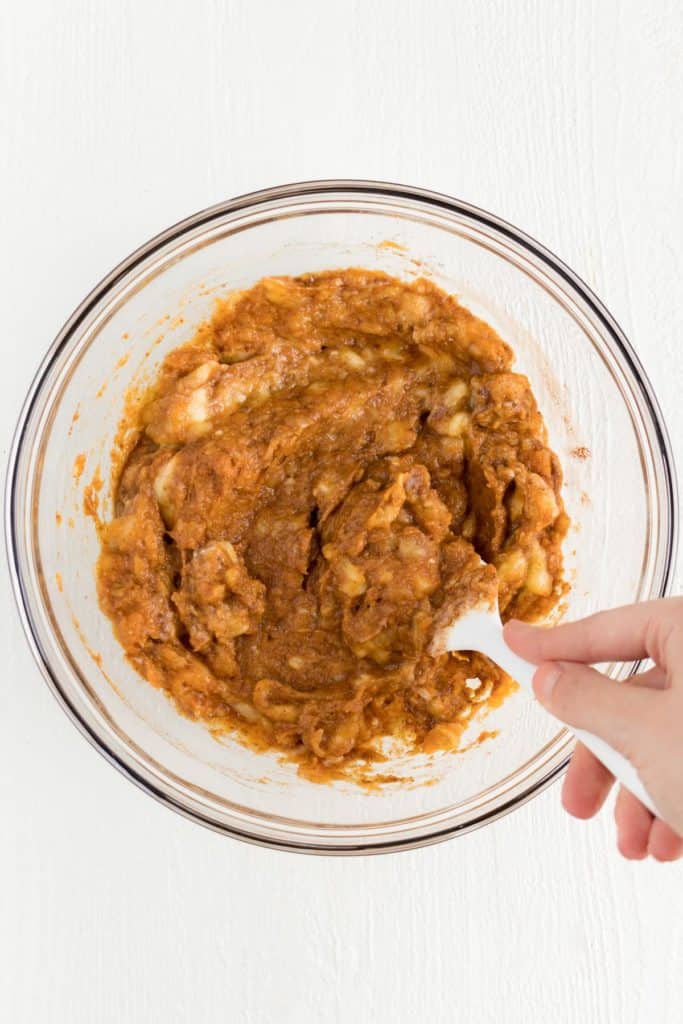 hand holding a white spatula mixing together pumpkin batter