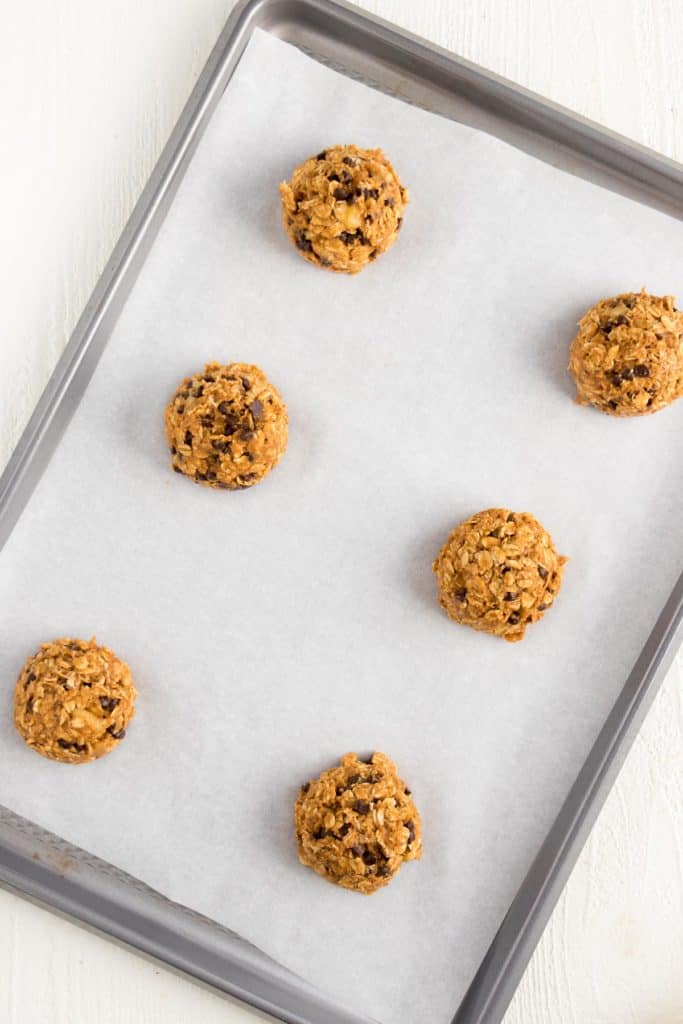 six balls of cookie dough on a metal baking sheet