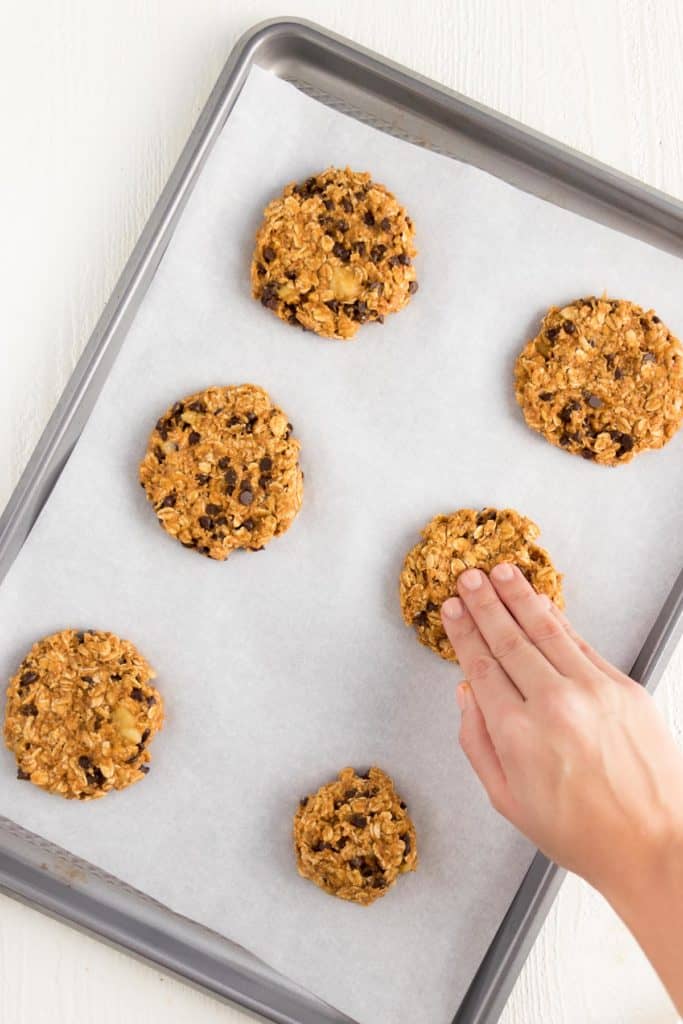 hand forming six chocolate chip pumpkin cookies on a baking sheet