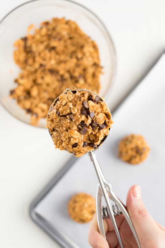 hand holding a large metal cookie scoop filled with pumpkin cookie dough