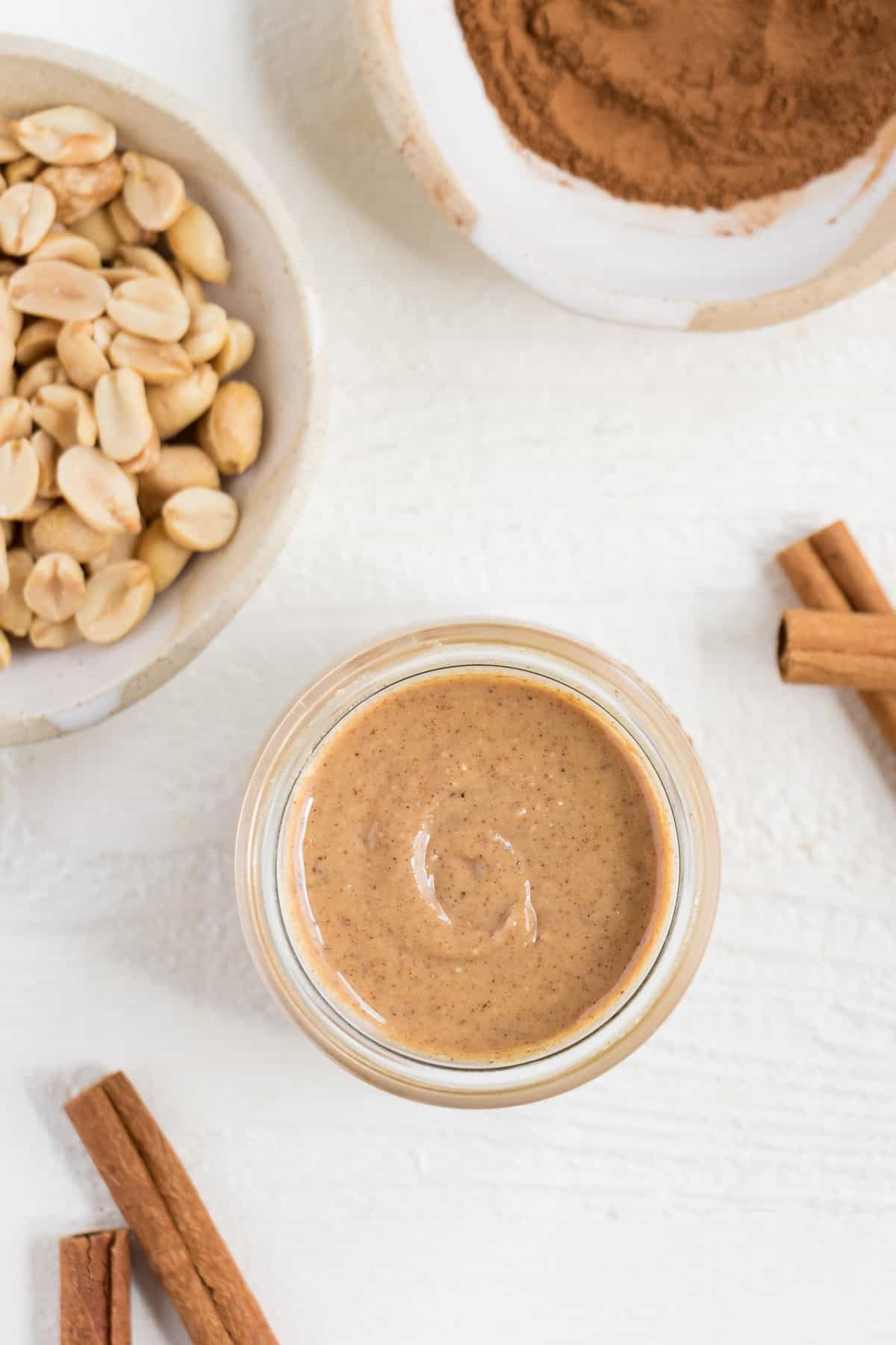 overhead image of peanuts, cinnamon, and homemade creamy peanut butter inside a glass jar