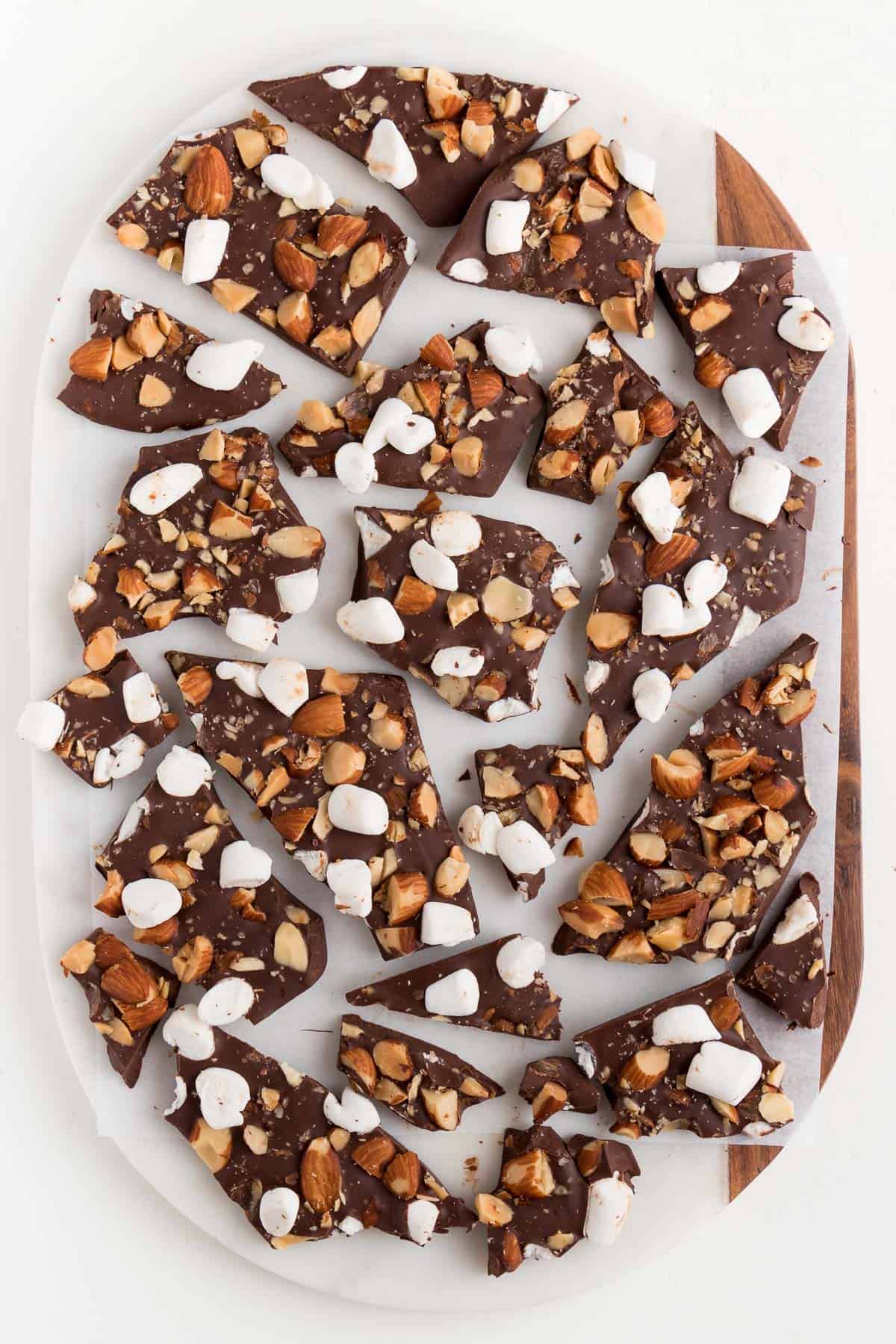 pieces of chocolate bark with almonds and marshmallows on top of a white marble and wood cutting board