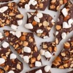 pieces of rocky road chocolate bark with marshmallows and almonds laying on a white surface