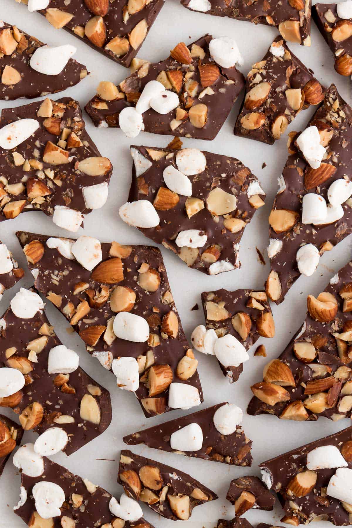 pieces of rocky road chocolate bark with marshmallows and almonds laying on a white surface