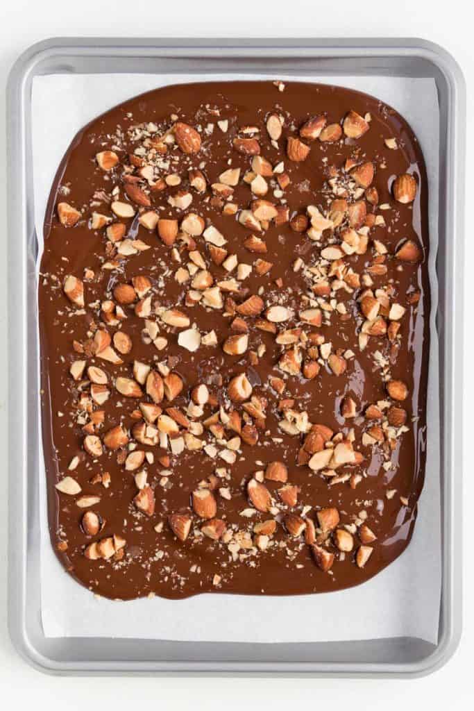 melted chocolate spread across a silver baking sheet topped with chopped almonds