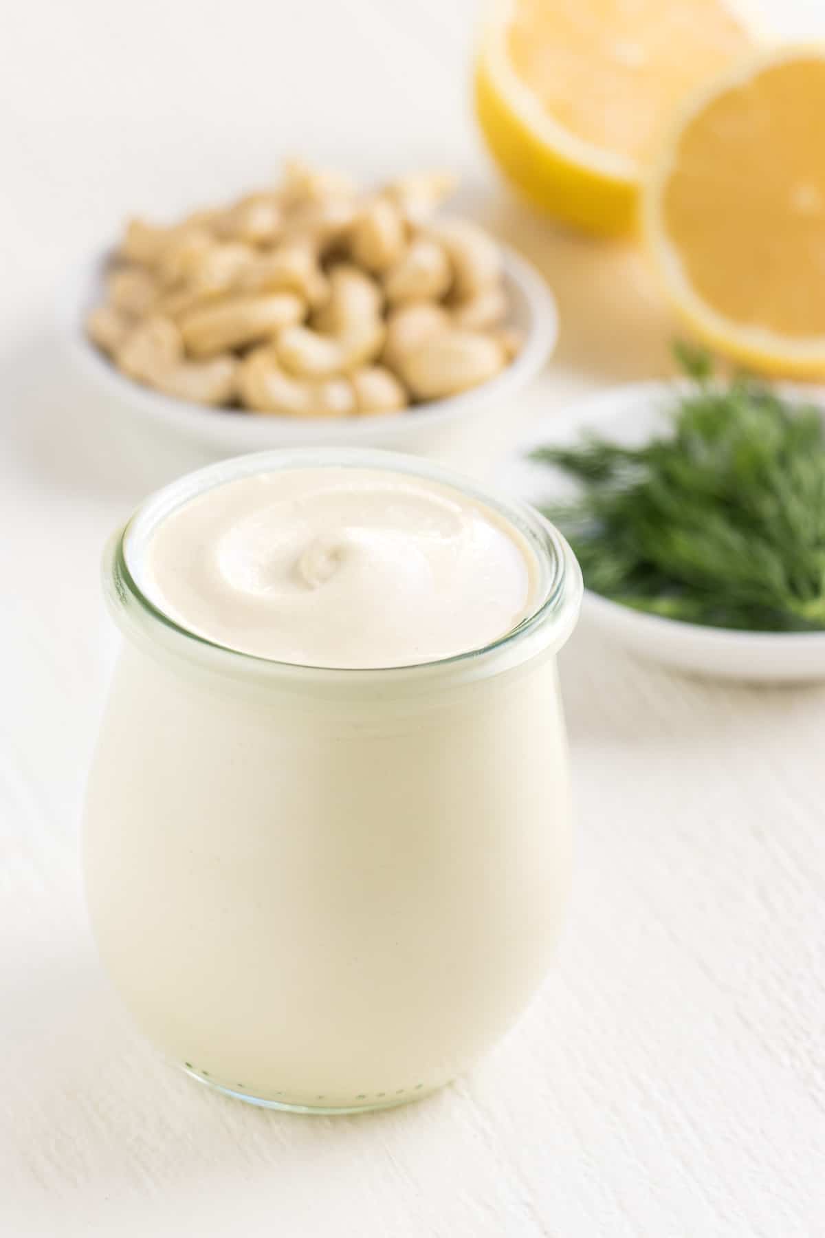 vegan cashew sour cream inside a glass jar surrounded by dill, lemon, and cashews