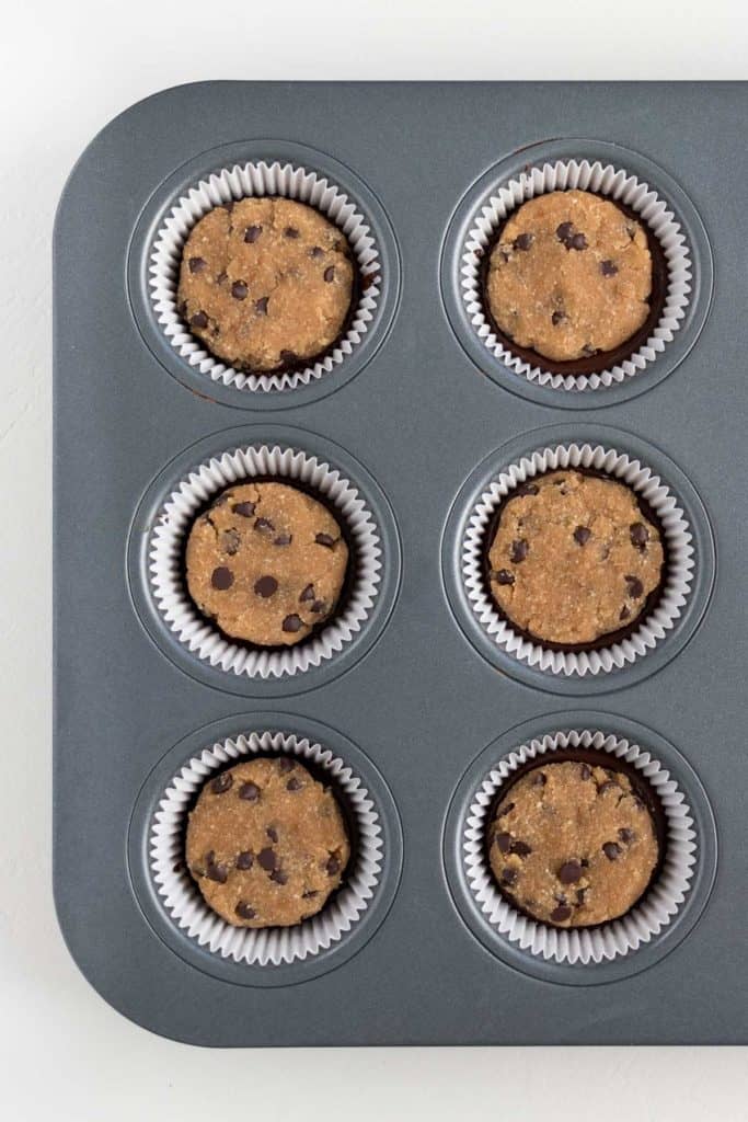 metal muffin tin containing white muffin liners filled with vegan no bake chocolate chip cookie dough
