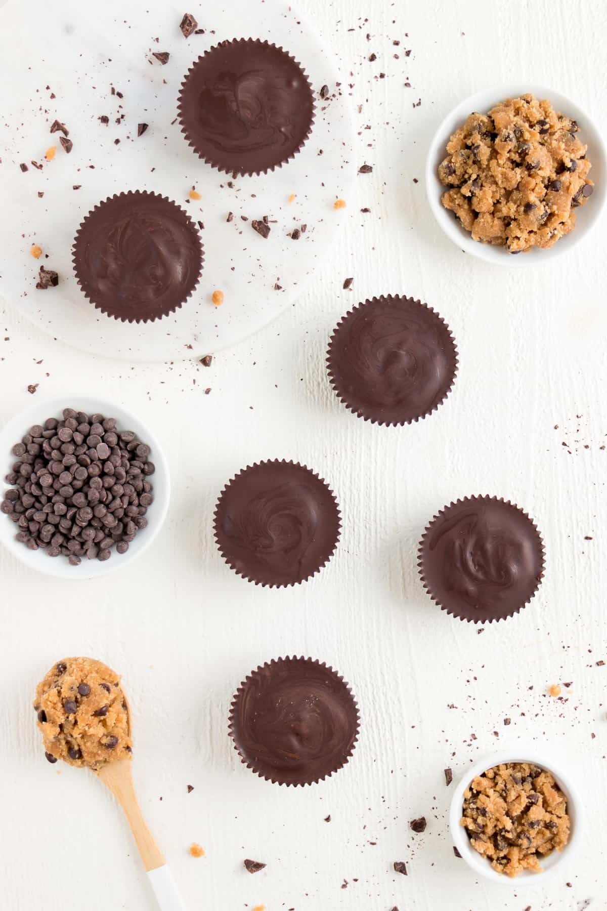 chocolate covered cookie dough cups surrounded by a wooden spoon, chocolate chips, and no bake cookie dough