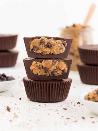 three stacked vegan chocolate chip cookie dough cups surrounded by chocolate chips