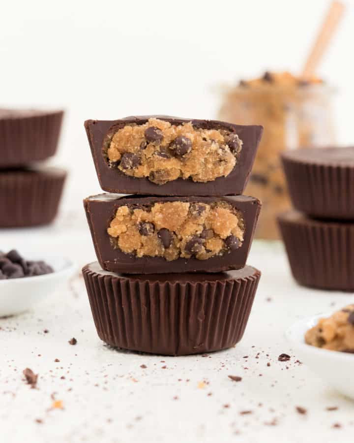 three stacked vegan chocolate chip cookie dough cups surrounded by chocolate chips