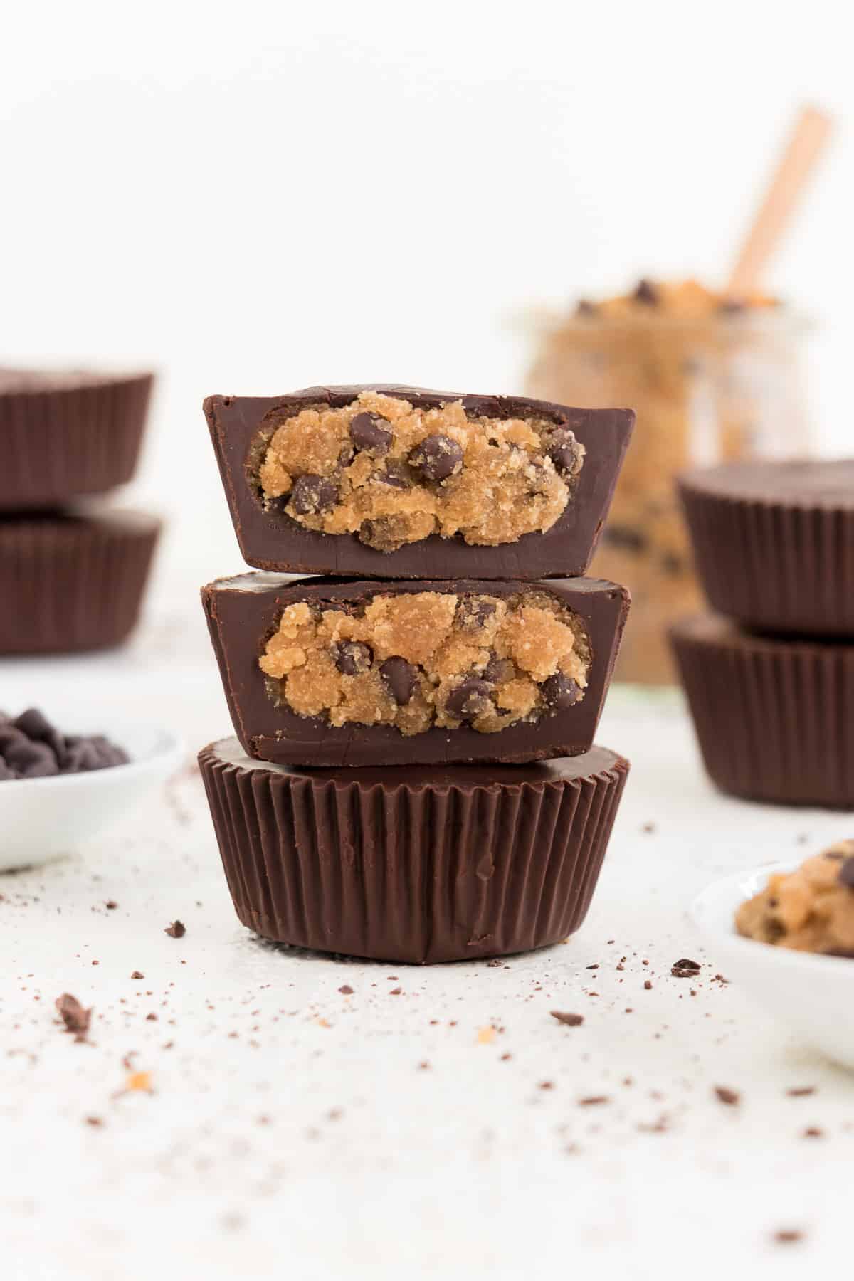 three stacked vegan chocolate chip cookie dough cups surrounded by chocolate chips