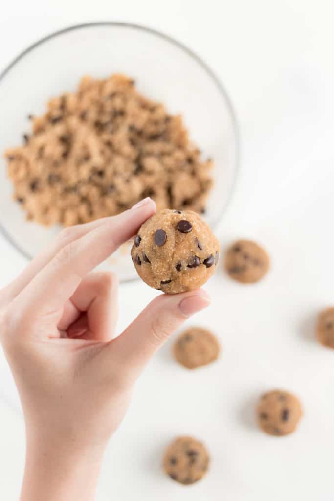 hand holding a rolled ball of vegan no bake chocolate chip cookie dough