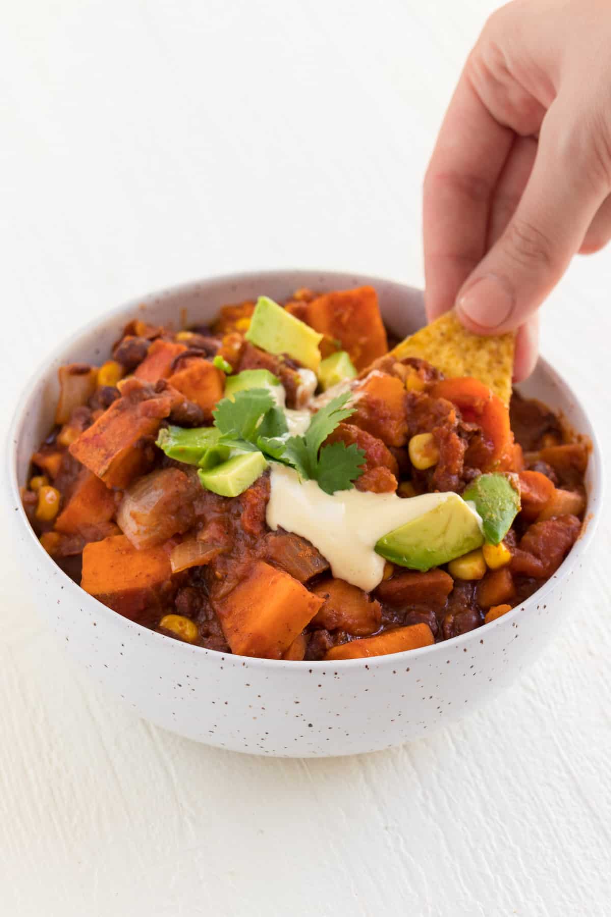 a hand holding a tortilla chip to scoop a bite of vegan chili