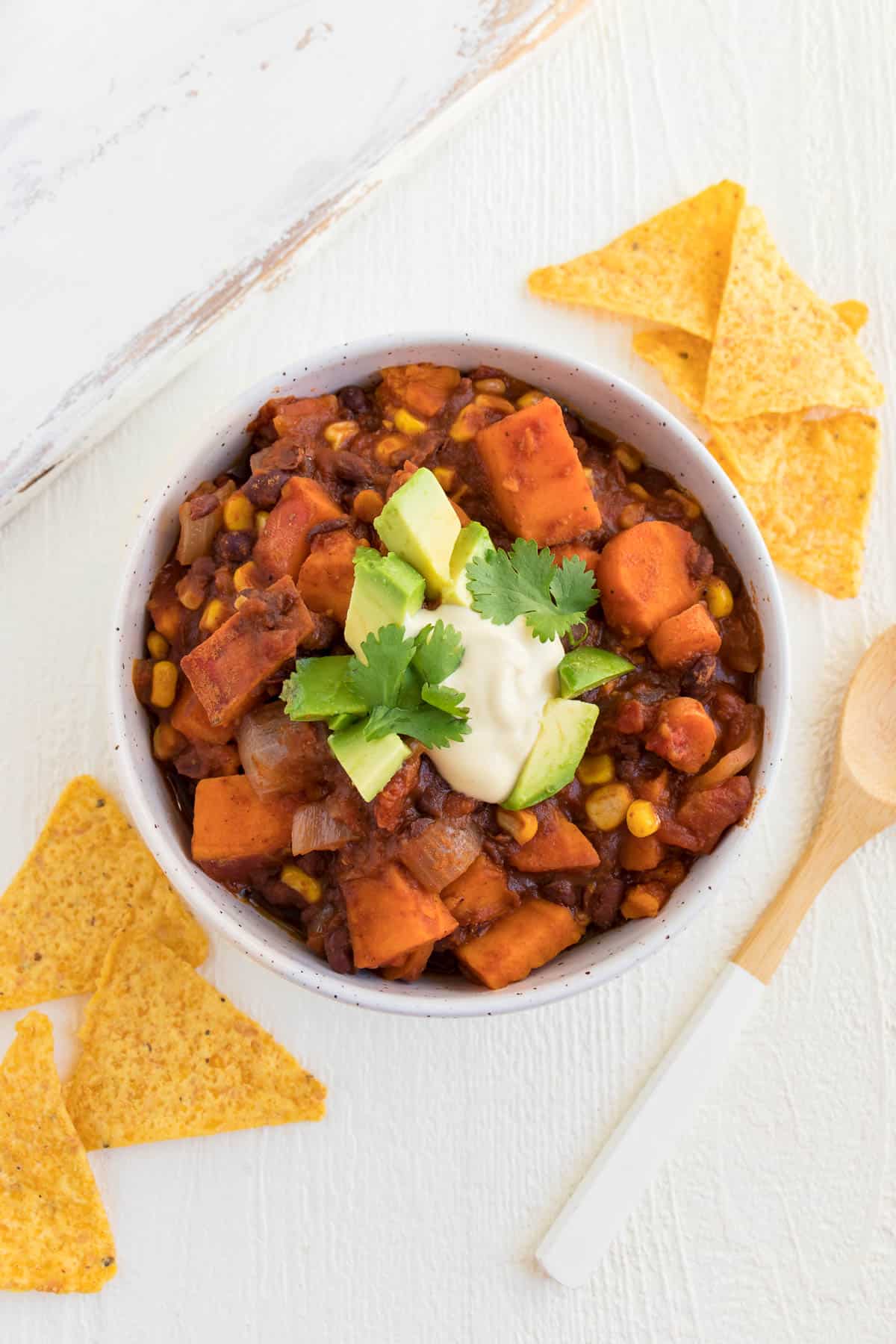 a bowl of vegan chili surrounded by a wooden bamboo spoon and corn tortilla chips