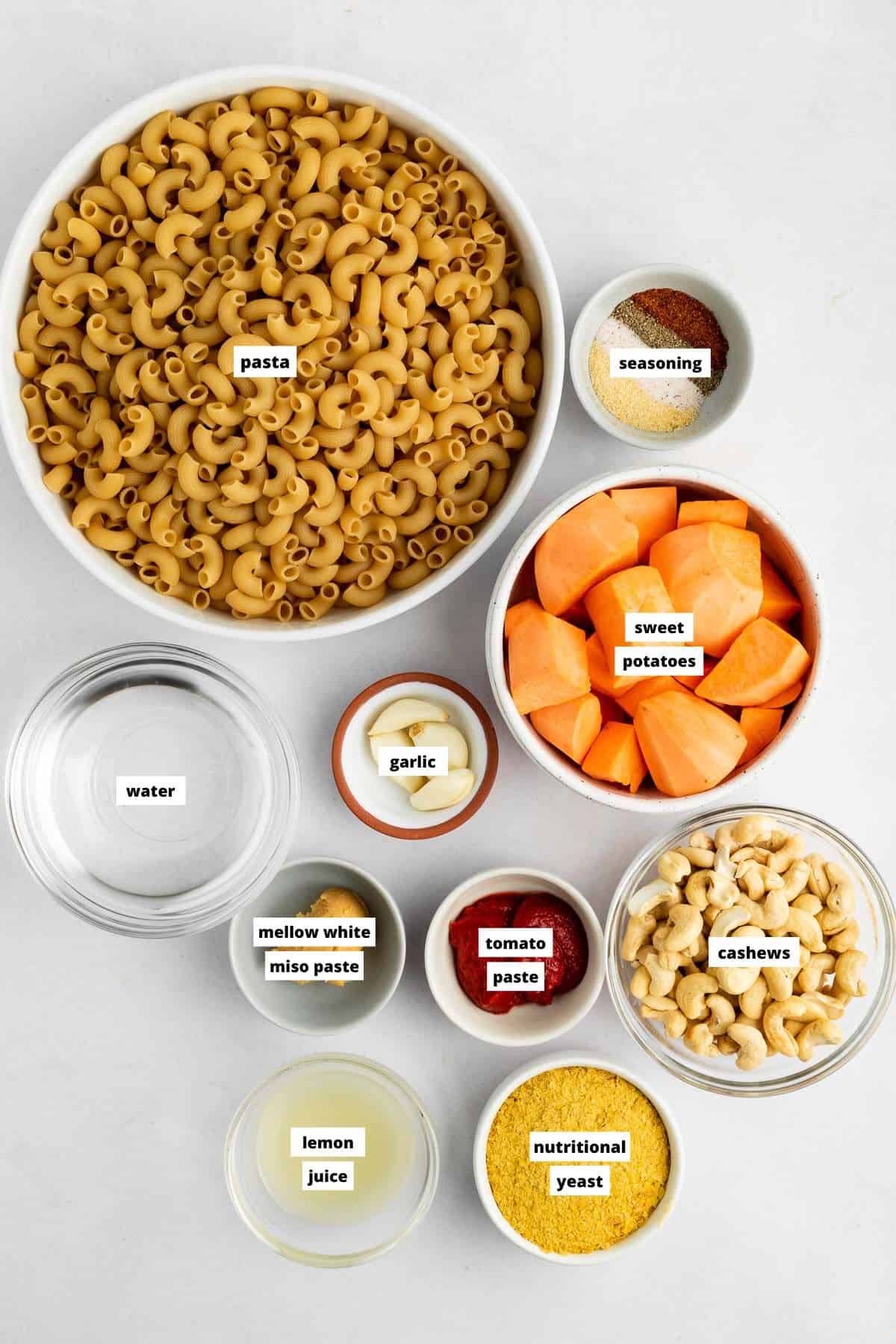 small white bowls with tomato paste, cashews, cubed sweet potato, lemon, garlic, and nutritional yeast on top of a marble wood cutting board 