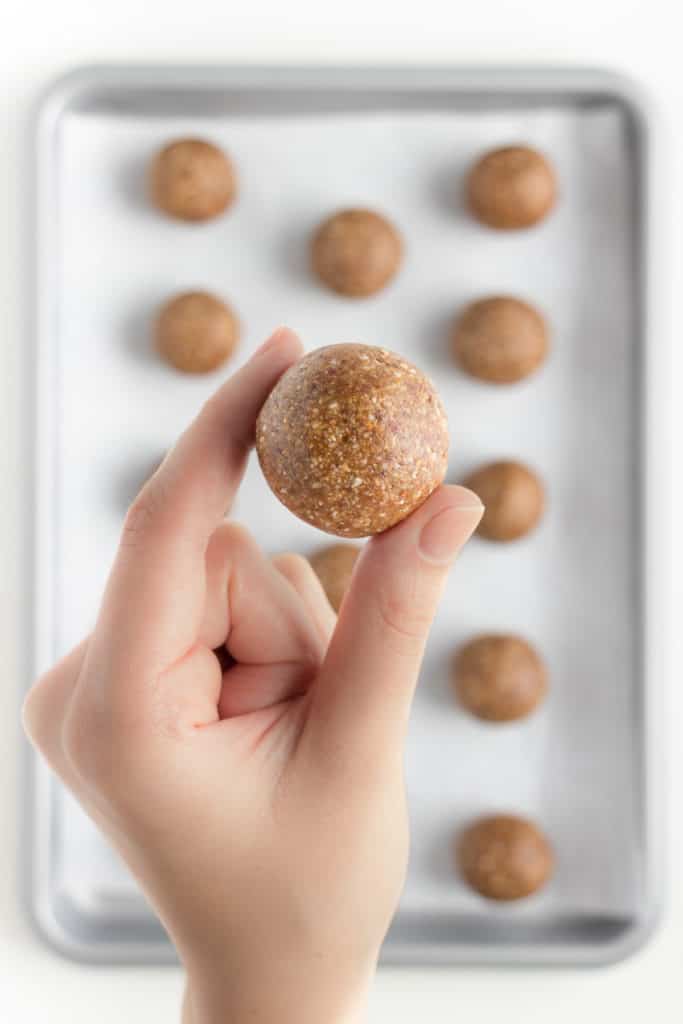 left hand holding a ball of no-bake gingerbread cookie dough in front of a silver baking sheet