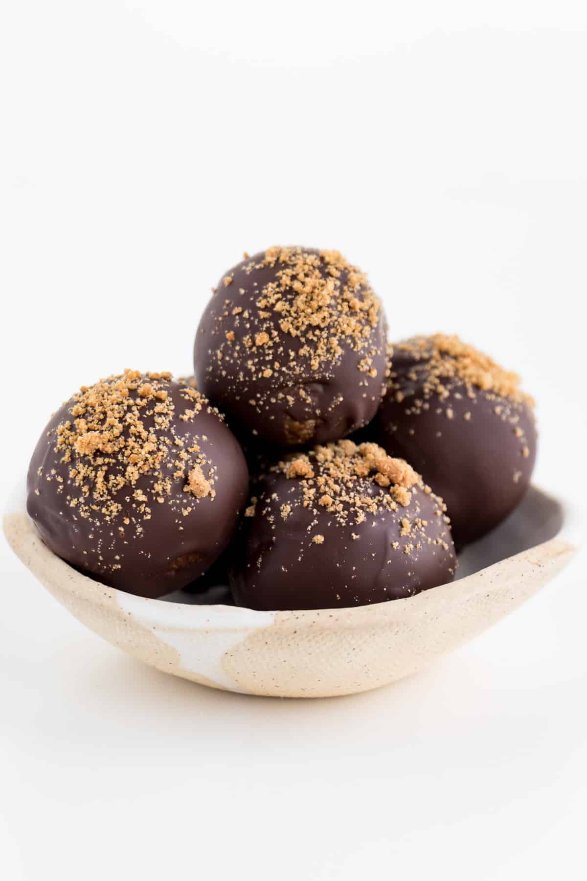 four chocolate gingerbread bliss balls stacked inside a cream and white ceramic bowl