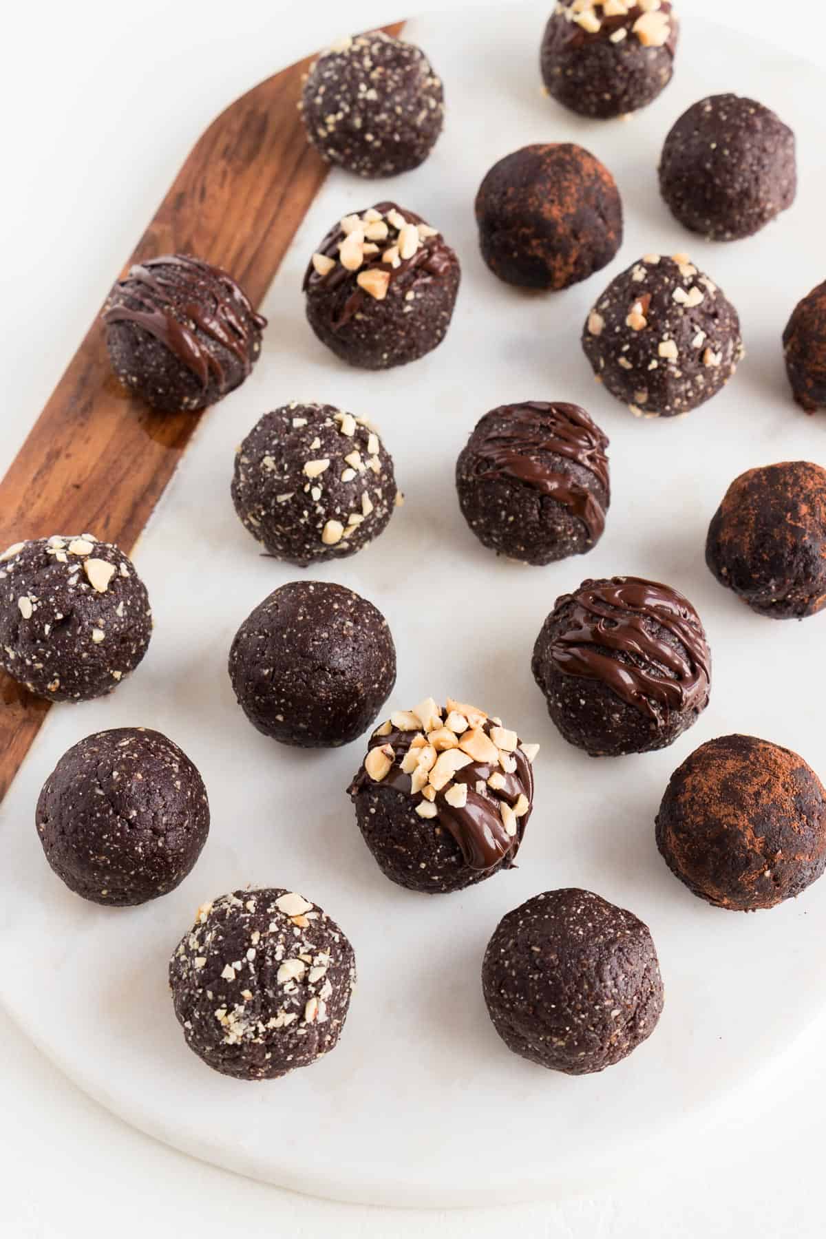 chocolate peanut butter energy balls sitting on top of a white marble and wood cutting board