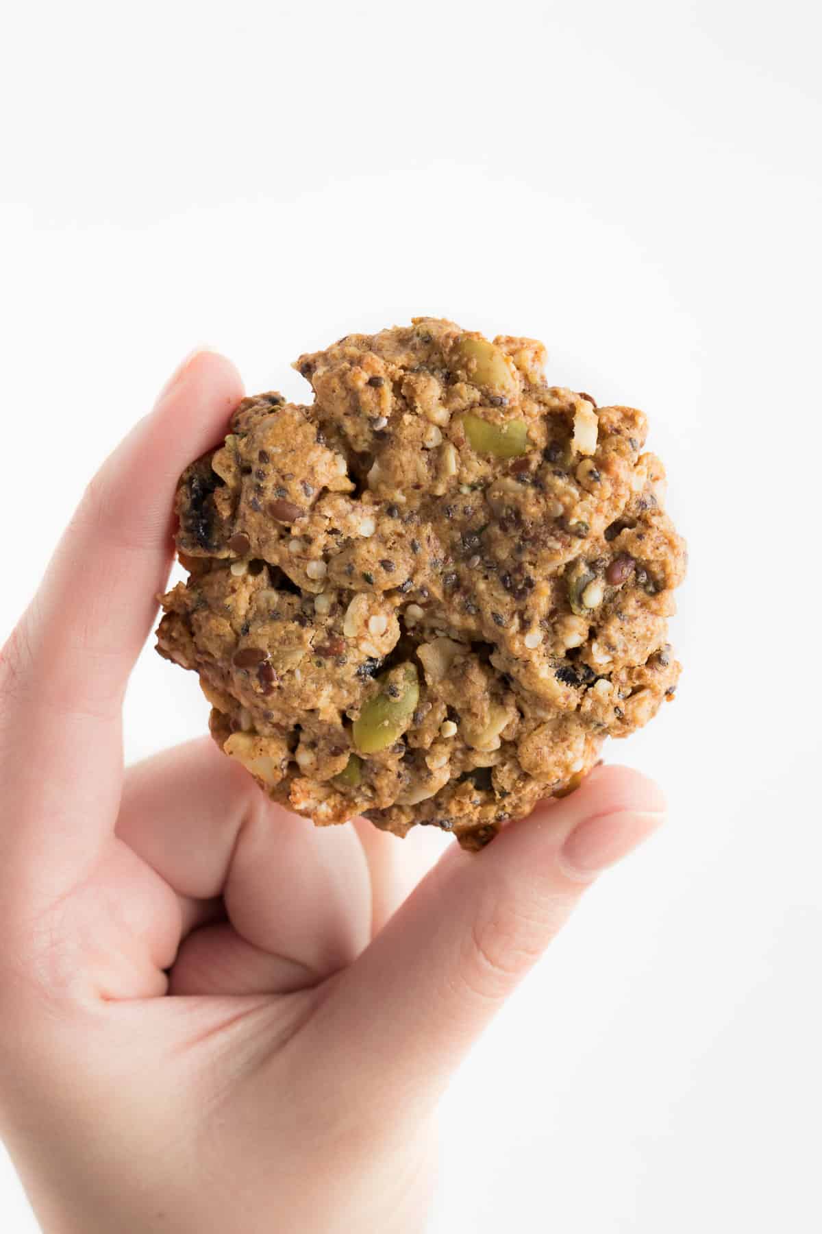 hand holding a vegan superfood breakfast cookie filled with pumpkin seeds, chia seeds, and cranberries