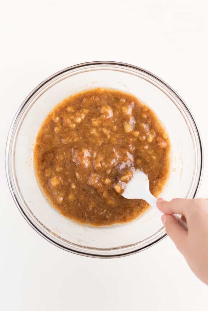 hand holding a white spatula mixing wet ingredients for banana bread